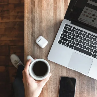 Una persona leyendo notas junto a un portátil y un café: un CTO lee tu brief